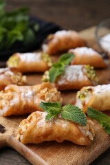 Delicious cannoli with cheese, nuts, powdered sugar and mint on table, closeup