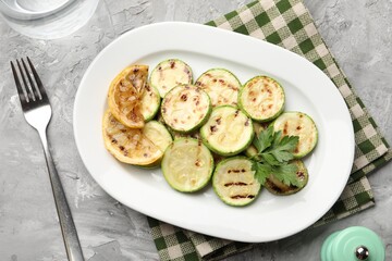 Delicious fried courgette slices with lemon and parsley served on grey table, flat lay