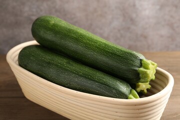 Fresh ripe zucchinis in wicker basket on wooden table, closeup