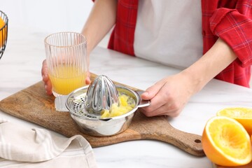 Woman with freshly squeezed orange juice and juicer at white marble table indoors, closeup
