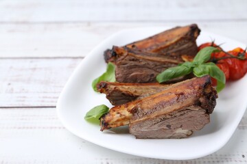 Roasted beef ribs, tomatoes and basil on white wooden table, closeup