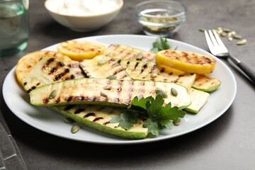 Delicious grilled courgette slices with pumpkin seeds, lemon and parsley on grey table, closeup