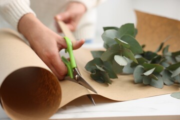 Florist making beautiful bouquet of eucalyptus branches at white table in flower shop, closeup