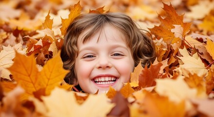 Joyful young child with a big smile peeking out from a pile of vibrant autumn fall leaves during the golden hour