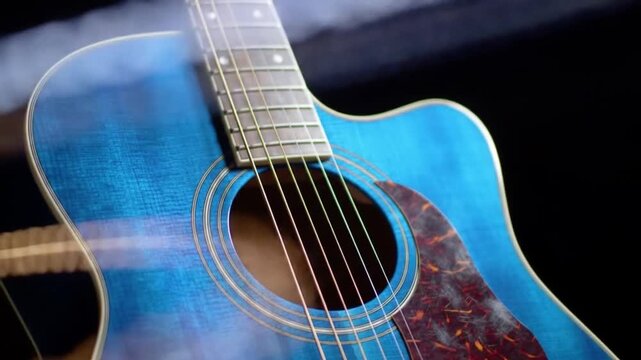Closeup of a vibrant blue acoustic guitar with sunburst pickguard on black.