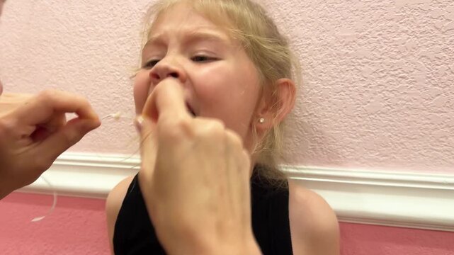 Close-up video of mother pulling out young girl&rsquo;s loose baby tooth using dental floss string at home, showing childhood milestone, dental care, parenting moment, oral hygiene, and family scene