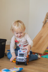 Blond little boy wearing Christmas shirt playing with toy car in festive kids room