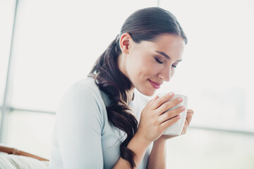 Charming woman enjoying a warm beverage in a bright and cozy living space, feeling relaxed and content during daytime