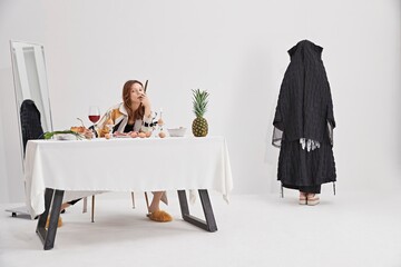 Woman in stylish attire contemplating at a dining table with food.