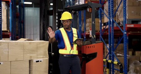 male african american warehouse inspector in yellow helmet and reflective vest holding tablet pointing upward while talking beside forklift during inventory control in logistic cargo distribution area - Powered by Adobe