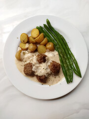 Meatballs smothered in creamy mushroom sauce with potatoes and green beans isolated on a white background. Perfect for a comforting meal.