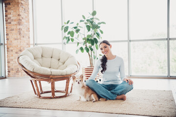 Fototapeta premium Cozy indoor scene with a cheerful woman relaxing at home, sitting with her dog on a rug, surrounded by warm decor