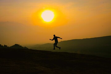 Silhouette of a person joyfully jumping against a glowing golden sunset over the hills, representing freedom, adventure, energy, and the beauty of nature
