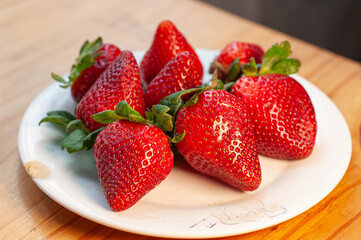 frutillas en un plato en la cocina frente a la ventana iluminada. fresas rojas en un cuenco sobre la mesa.