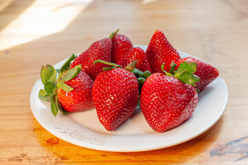 frutillas en un plato en la cocina frente a la ventana iluminada. fresas rojas en un cuenco sobre la mesa.
