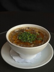 Traditional Chinese egg drop soup with mushrooms, chili oil and fresh green onions in white bowl. Concept of comfort food, Asian flavors, homemade dishes and healthy hot meals.
