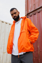 Stylish african american man in orange windbreaker jacket standing in cargo port  © Dmytro Hai