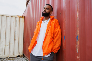 African american man in windbreaker jacket standing near cargo container in port  © Dmytro Hai
