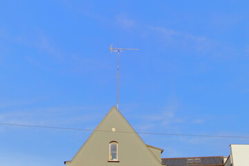 Old house roof with a TV antenna against clear blue sky.