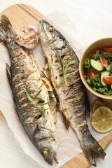 Tasty roasted seabass fish served with salad and lemon on white wooden table, top view. Homemade seafood dish