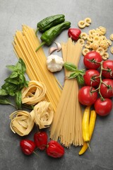 Different types of raw pasta and products on grey textured table, flat lay