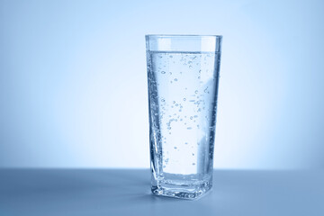 Refreshing soda water in glass on table against light blue gradient background, closeup