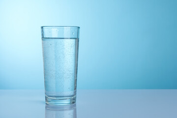 Refreshing soda water in glass on light grey mirror table against turquoise gradient background, closeup. Space for text