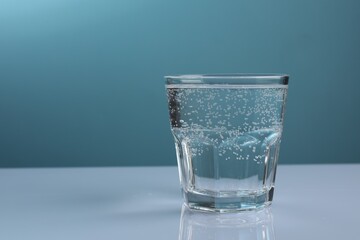 Refreshing soda water in glass on white mirror table against dark turquoise background, closeup. Space for text