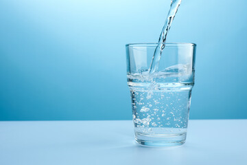 Pouring refreshing soda water into glass at white table against light blue gradient background, closeup. Space for text