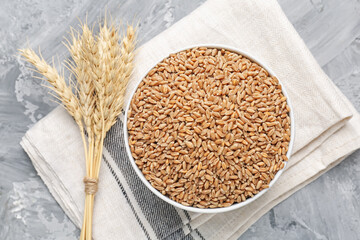 Wheat grains in bowl and spikes on grey table, flat lay