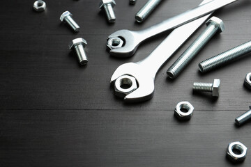 Many metal wrenches, bolts and nuts on black wooden table, above view. Space for text