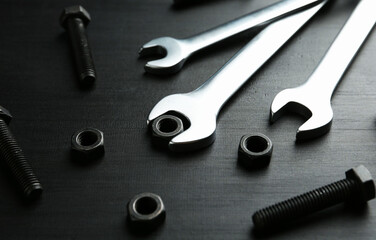 Many metal wrenches, bolts and nuts on black wooden table, closeup