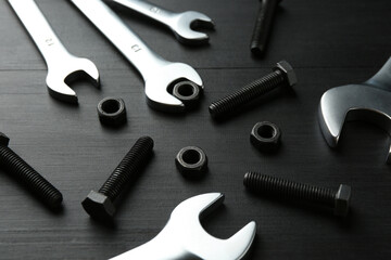 Many metal wrenches, bolts and nuts on black wooden table, closeup