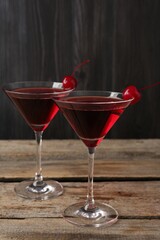 Martini cocktail with cherries in glasses on wooden table, closeup