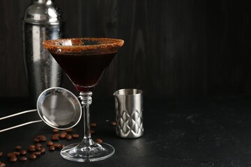 Martini cocktail with sugar in glass, coffee beans and shaker on black table, closeup. Space for text