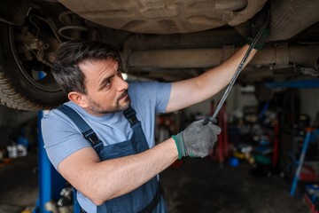 Car mechanic repairing a lifted car in a workshop