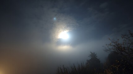 Night sky with full moon shining through clouds and fog creating a mystical and atmospheric scenery view