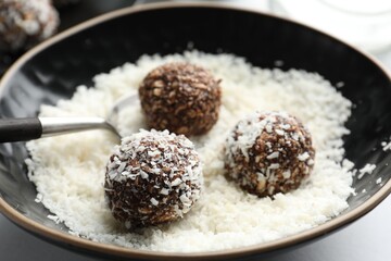 Making tasty chocolate candies with nuts and coconut flakes at white table, closeup