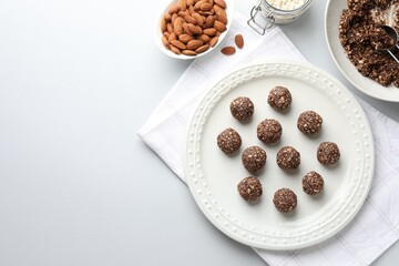 Tasty chocolate candies with nuts and ingredients on white table, flat lay. Space for text
