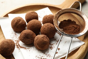 Tasty chocolate candies with cocoa powder and strainer on light table, closeup