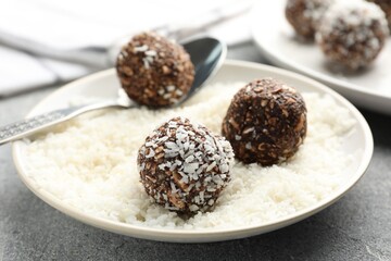 Making tasty chocolate candies with coconut flakes at grey table, closeup