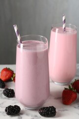 Tasty milkshakes in glasses and berries on white marble table, closeup
