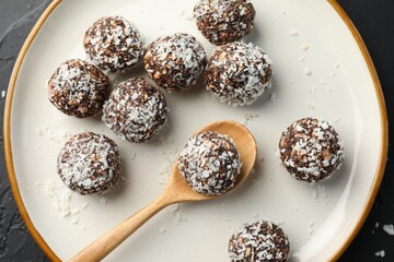 Tasty chocolate candies with nuts and coconut flakes on black table, top view