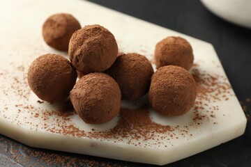 Tasty chocolate candies with cocoa powder on black table, closeup