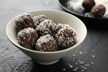 Tasty chocolate candies with nuts and coconut flakes in bowl on black table, closeup