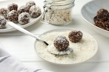 Tasty chocolate candies with nuts, coconut flakes and puffed rice on white wooden table, closeup
