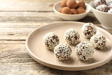 Tasty chocolate candies with nuts and sesame seeds on wooden table, closeup