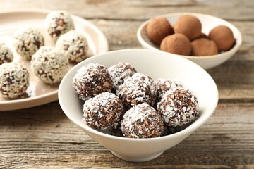 Tasty chocolate candies with coconut flakes, nuts, sesame seeds and cocoa powder on wooden table, closeup