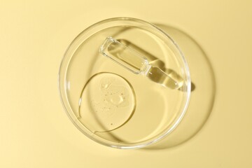 Glass ampoule with liquid and Petri dish on yellow background, top view