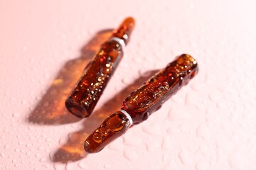 Glass ampoules with liquid and water drops on pink background, closeup